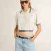 Kropptes, in Weiss geträgertes Damen-Polohemd aus Baumwolle mit blauen Rippbündchen